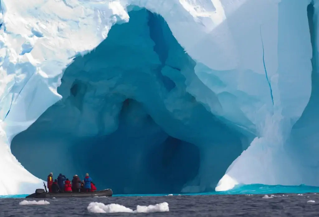 Expedition boat beside a sculpted iceberg in the Southern Ocean