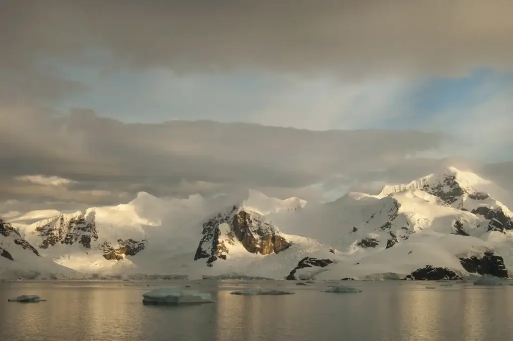 Calm Antarctic water reflecting snow-covered mountains at dusk