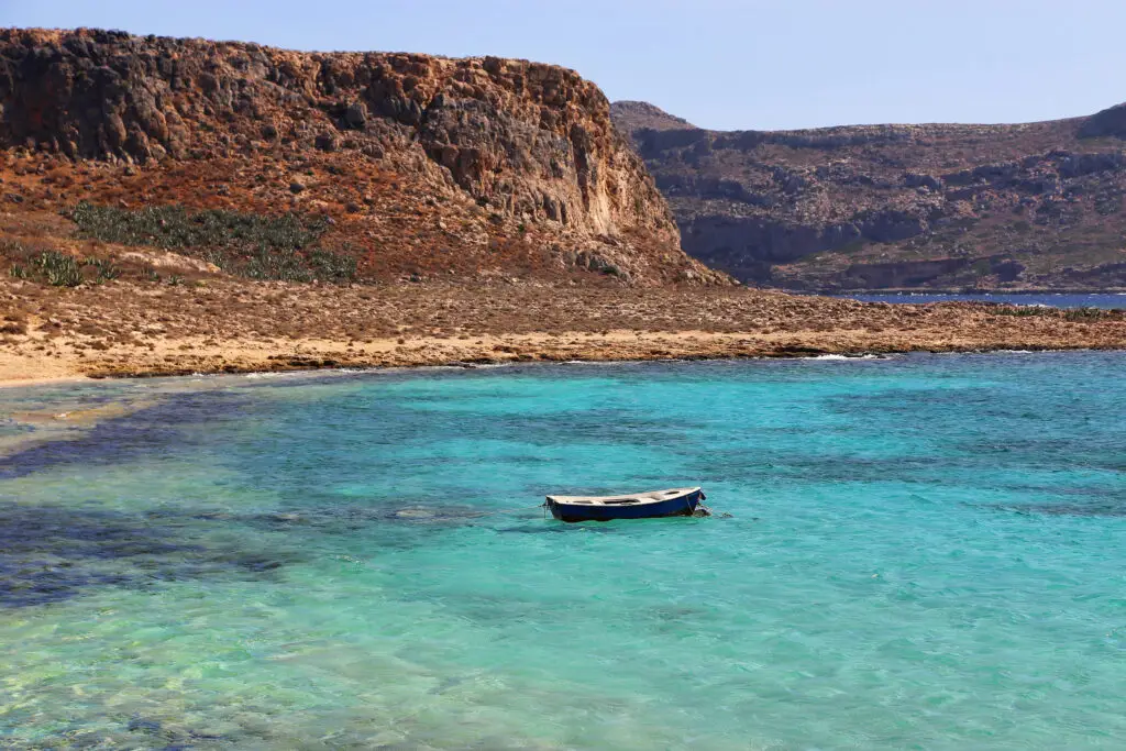 Small boat in clear turquoise water beside the Cretan coast