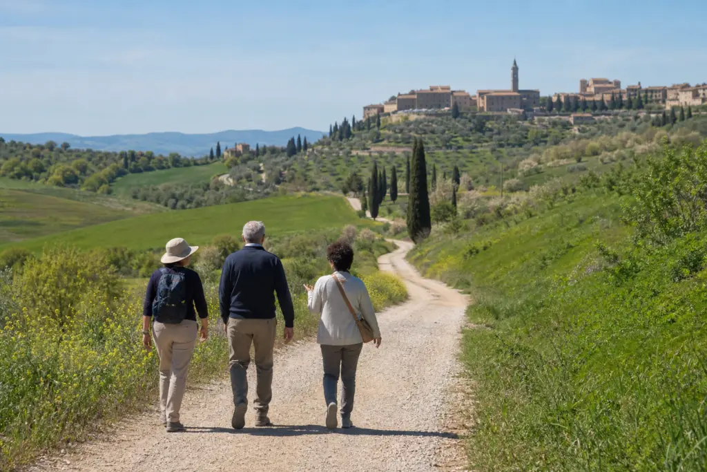 Two travelers and a local guide walking a rural Via Francigena route in Tuscany