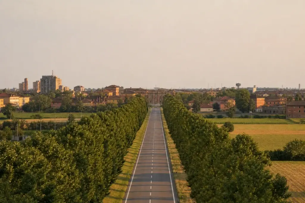 Straight tree-lined road approaching a historic city edge in a non-specific Via Emilia route concept