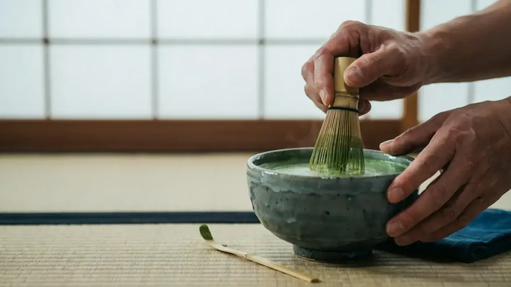Hands whisking matcha in a ceramic bowl during Japanese tea practice