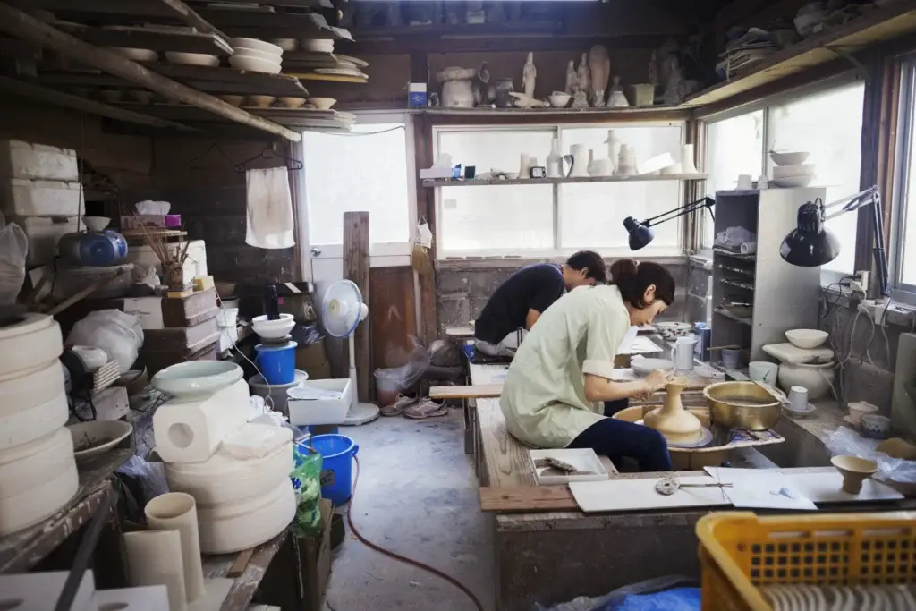 Woman working in a Japanese porcelain workshop, sitting at a potter's wheel, throwing bowl.