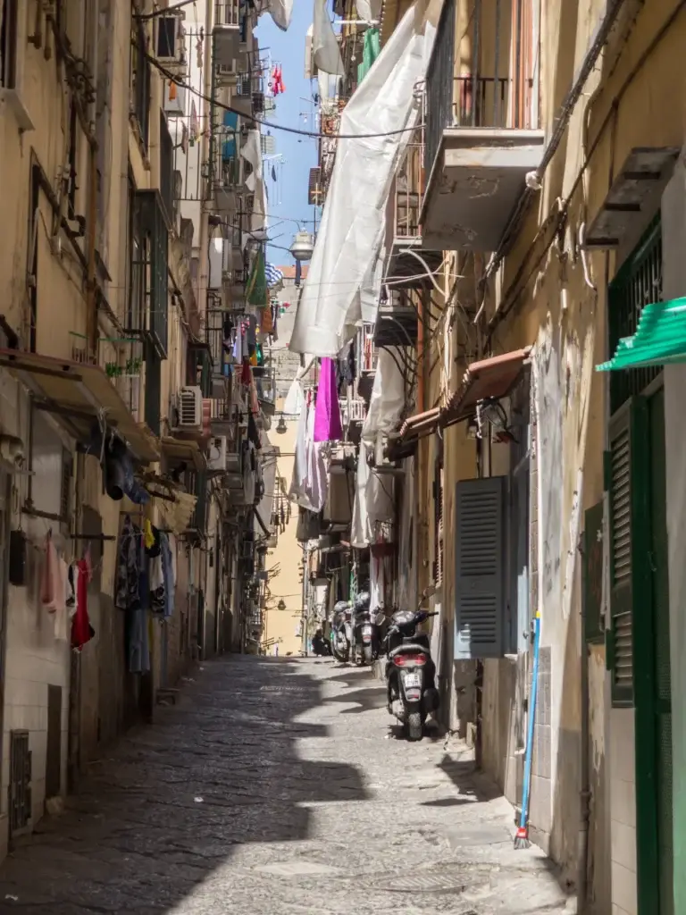 Narrow cobblestone street with laundry and scooters in Naples