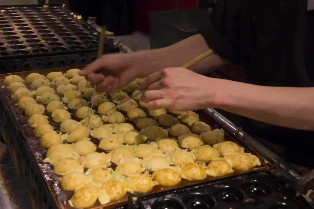 Cook turning takoyaki in a traditional Japanese pan