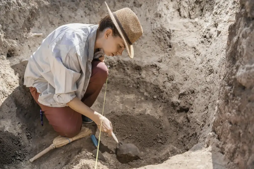 Archaeologist carefully excavating a field site with small tools