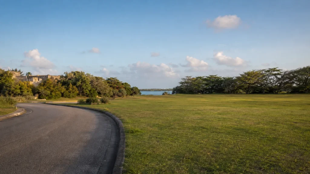 AI visualization of an anonymous curving street, open grass and distant protected harbor water in a Bridgetown context