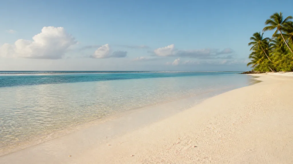 AI-generated editorial visualization of Tikehau's pale coral-sand shoreline with only a restrained non-uniform blush undertone; not an exact motu, beach, ecology, access, sand color, weather or current-condition record.