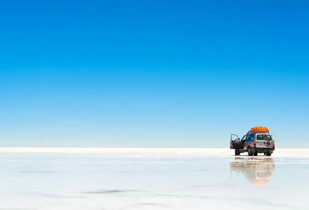 A vehicle provides scale on a reflective surface of the Salar de Uyuni.
