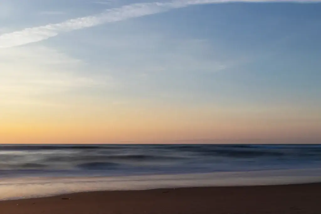 Long Exposure Of Waves Crashing Up On The Beach Shore At Sunrise Looking East